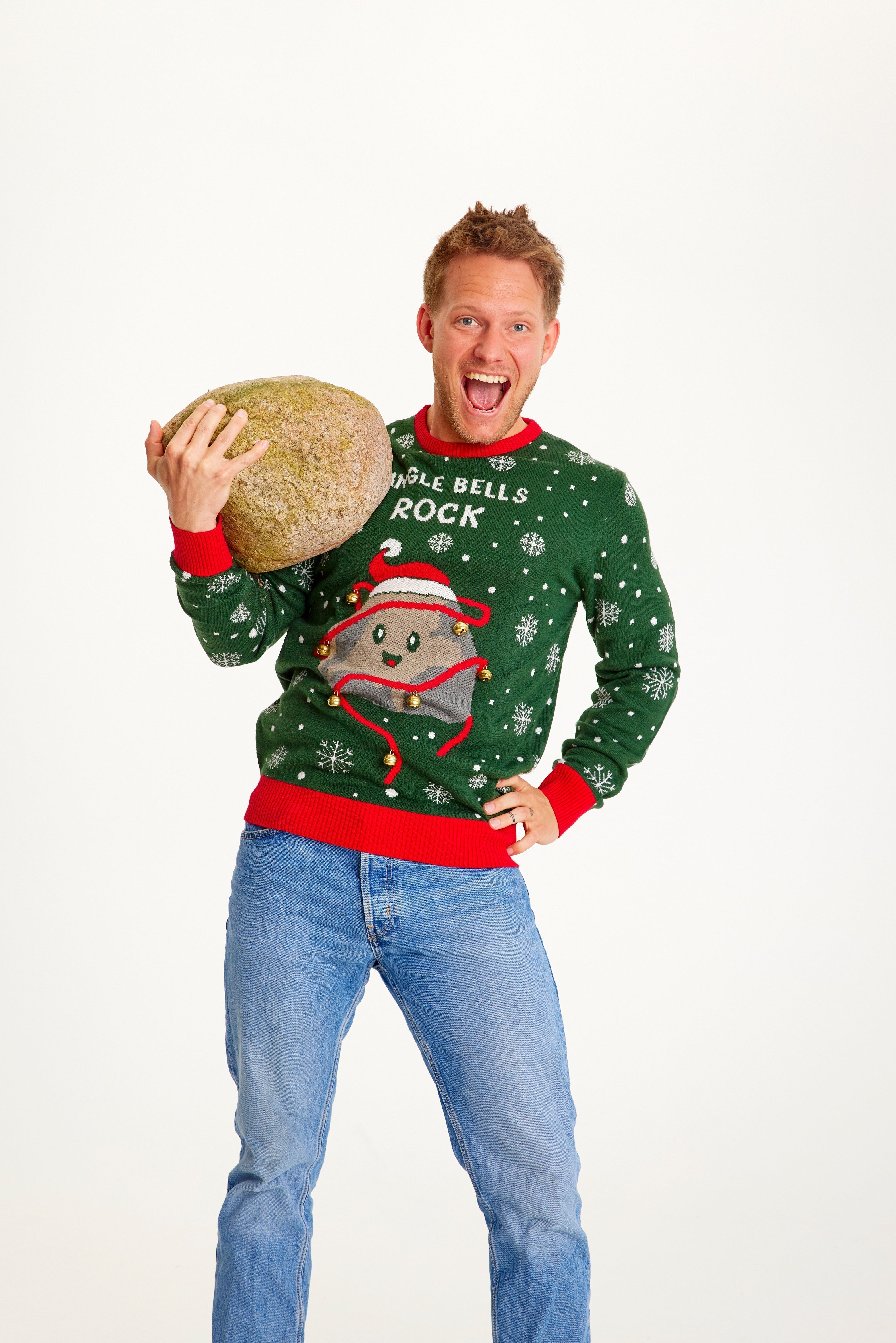 Un homme pose avec une pierre, vêtu d'un pull vert de Noël orné d'une pierre.